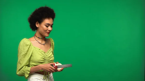 Mujer afroamericana complacida sosteniendo auriculares aislados en verde - foto de stock