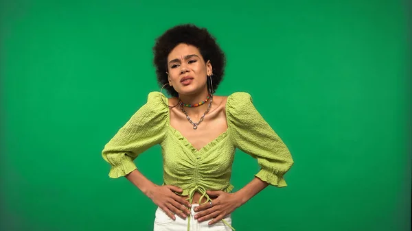 Mujer afroamericana insatisfecha en pendientes de aro con dolor de estómago aislado en verde - foto de stock