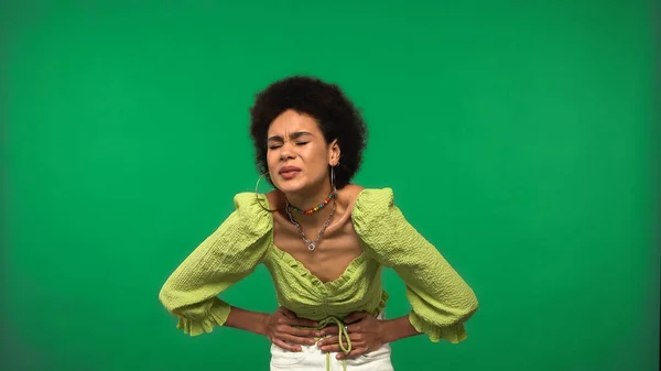 Mulher afro-americana em blusa com dor de estômago isolada em verde — Fotografia de Stock