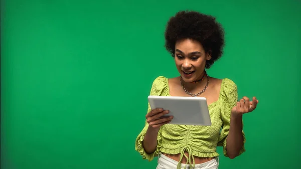 Femme afro-américaine gaie en chemisier en utilisant une tablette numérique isolé sur vert — Photo de stock
