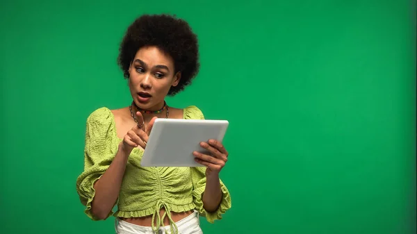 Surprised african american woman using digital tablet isolated on green — стоковое фото