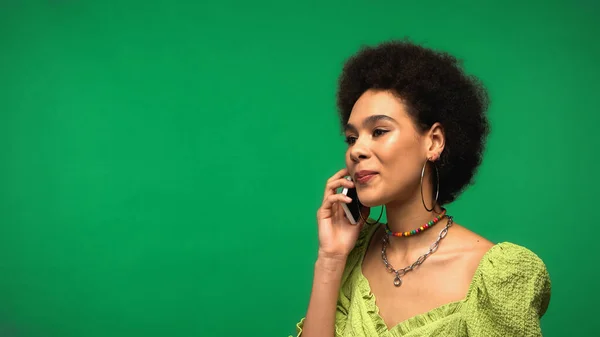 Encaracolado afro-americano mulher na blusa falando no smartphone isolado no verde — Fotografia de Stock