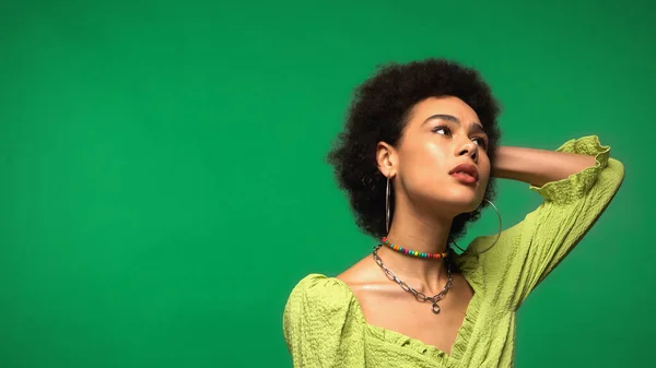 Pensive african american woman in hoop earrings looking away isolated on green — стоковое фото