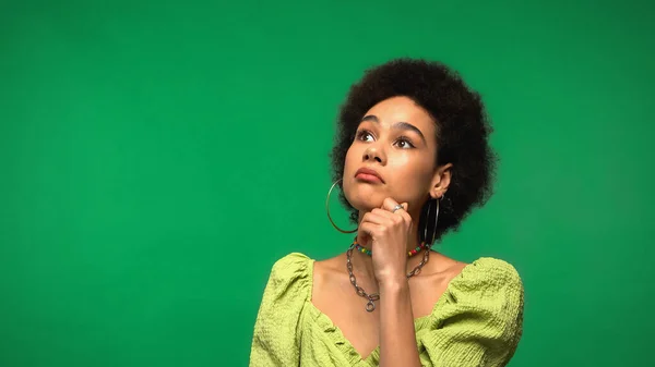 Mulher afro-americana pensativo em brincos de argola e blusa olhando para longe isolado em verde — Fotografia de Stock