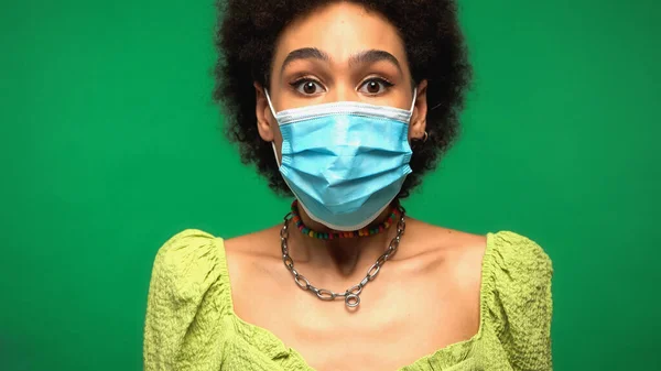 Mujer afroamericana asustada en máscara médica aislada en verde - foto de stock