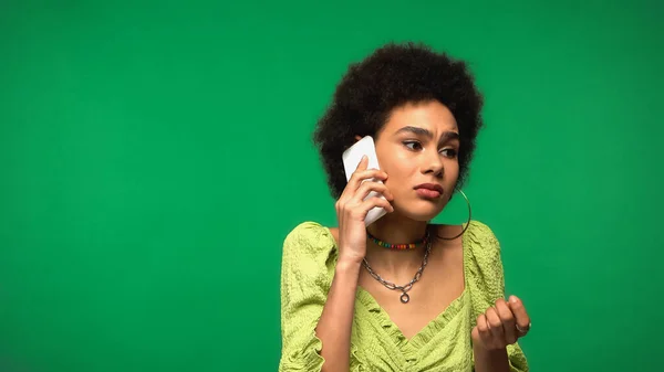 Upset african american woman in blouse talking on cellphone isolated on green — Stock Photo