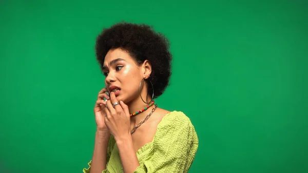 Обеспокоенная африканская американка в блузке разговаривает по сотовому, изолированному на зеленый — стоковое фото