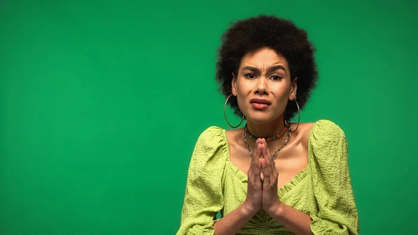 African american woman in hoop earrings standing with praying hands isolated on green — Foto stock