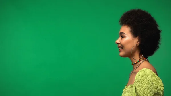 Side view of cheerful african american woman smiling isolated on green — стоковое фото