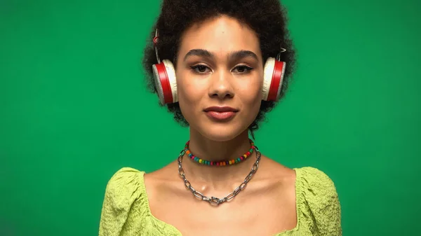 Young african american woman in wireless headphones listening music isolated on green — Foto stock