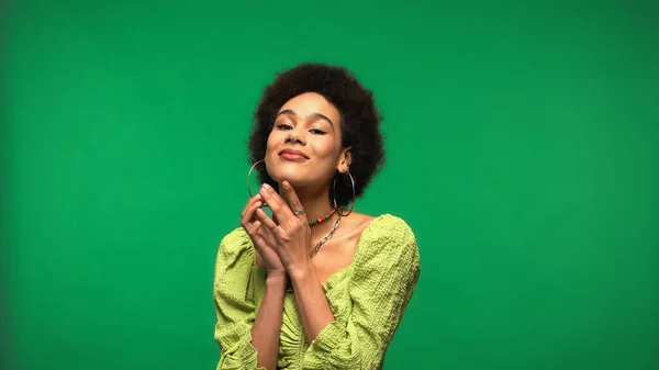 Positive african american woman in blouse and hoop earrings isolated on green — Stockfoto