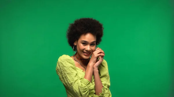 Joyful african american woman in blouse and hoop earrings smiling isolated on green — Stockfoto