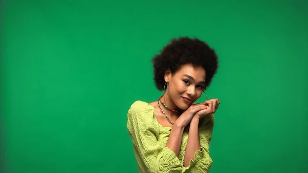 Cheerful african american woman in blouse and hoop earrings smiling isolated on green — Foto stock