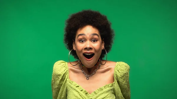 Animado afro-americano mulher em blusa e aro brincos olhando para a câmera com a boca aberta isolado no verde — Fotografia de Stock