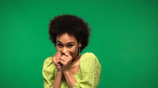 Shy african american woman in blouse covering face with hands isolated on green — Stockfoto