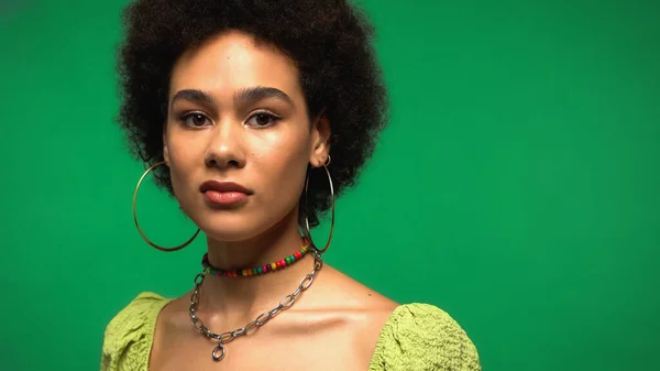 Mujer afroamericana disgustada en blusa y pendientes de aro aislados en verde - foto de stock