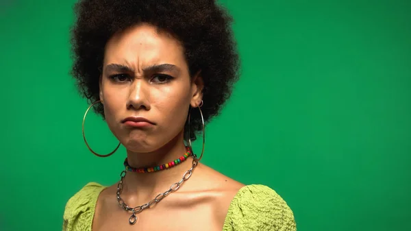 Frustrated african american woman in blouse and hoop earrings isolated on green — стоковое фото