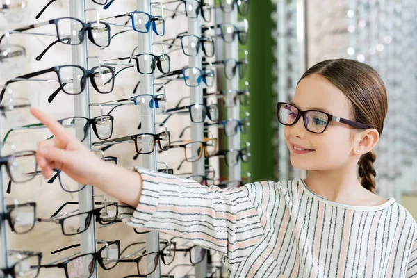 Positive child pointing at assortment of eyeglasses in optics shop — Foto stock