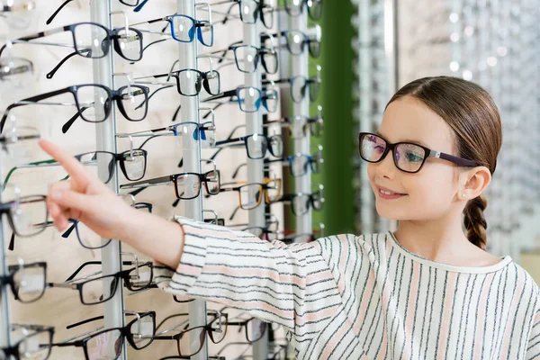 Positive child pointing at assortment of eyeglasses in optics shop — Stock Photo