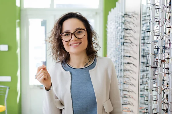 Happy woman in eyeglasses looking at camera in optics store — Stock Photo