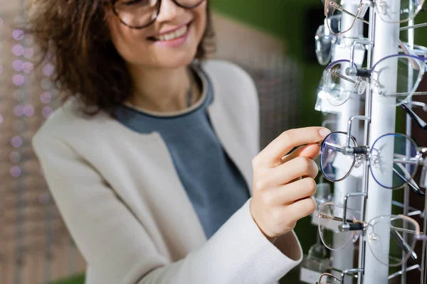 Cropped view of blurred smiling woman choosing eyeglasses in optics store — Stock Photo
