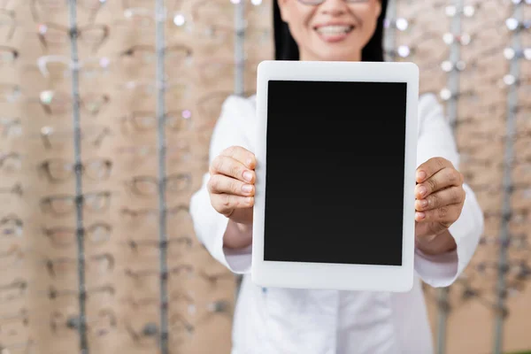 Vista recortada del oculista borroso mostrando tableta digital con pantalla en blanco en la tienda de óptica - foto de stock