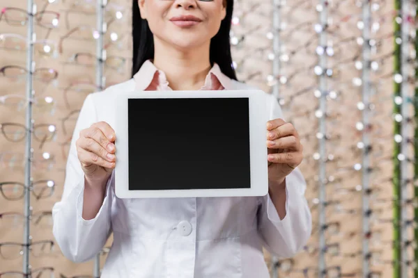 Cropped view of blurred oculist in white coat holding laptop with blank screen in optics salon — Stockfoto