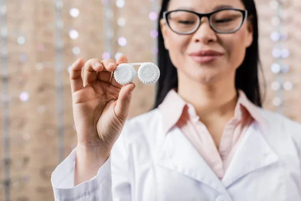 Blurred asian oculist in eyeglasses holding lens case in optics store — Stock Photo