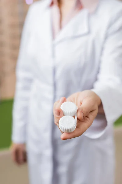 Partial view of blurred ophthalmologist holding lens case in optics shop - foto de stock