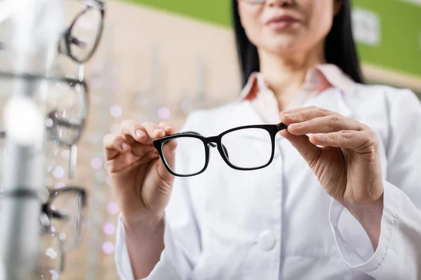 Обрізаний вид розмитого окуліста, який тримає окуляри під час роботи в магазині оптики — стокове фото