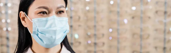 Asian ophthalmologist in medical mask in optics salon on blurred background, banner — Stock Photo