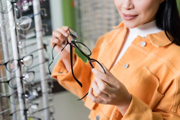 Cropped view of blurred woman comparing eyeglasses in optics shop — Stockfoto