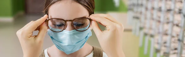 Oculist putting eyeglasses on girl in medical mask, banner — Stock Photo