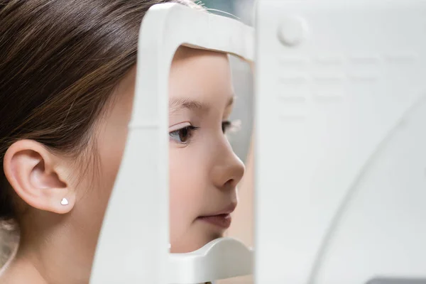 Girl measuring eyesight on blurred ophthalmoscope — Stock Photo