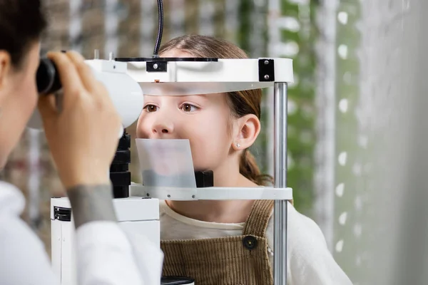 Blurred optometrist measuring eyesight of girl on vision screener in optics shop — Stockfoto