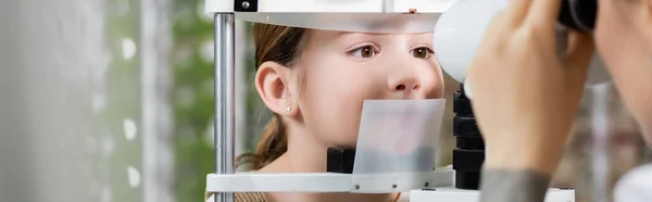 Borrosa oculista comprobación de la vista de la chica en la pantalla de visión en la tienda de óptica, pancarta - foto de stock