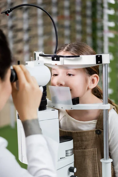 Optometrista borrosa prueba de la visión de la niña en autorefractor en el salón de óptica - foto de stock