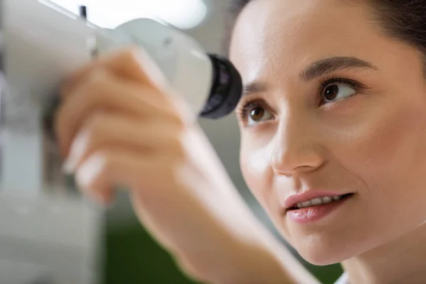 Young oculist tuning ophthalmoscope on blurred foreground — стоковое фото