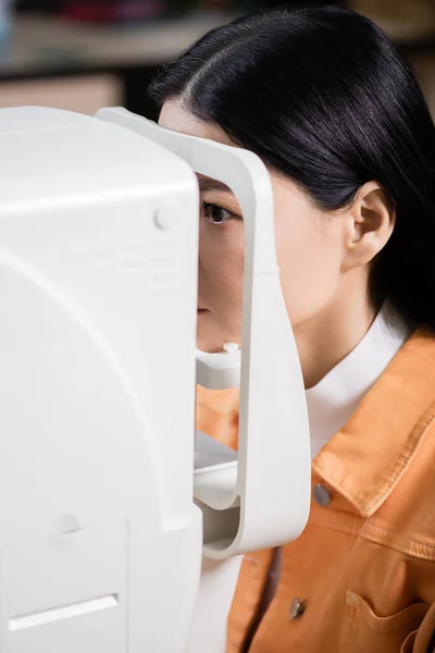 Asian woman examining eyesight on blurred ophthalmoscope — Stock Photo