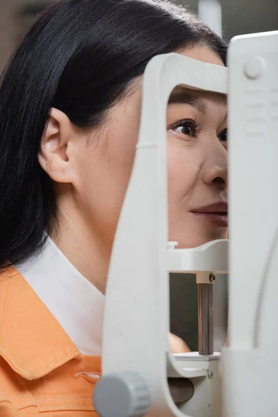 Азіатська жінка перевіряє зір на розмитому авторефракторі — стокове фото
