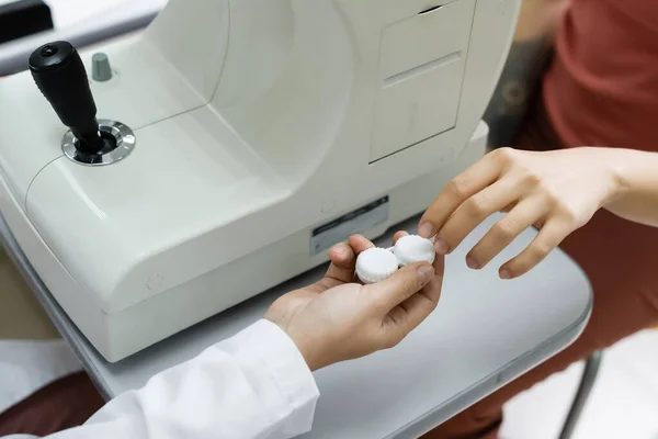 Partial view of optometrist giving lens case to patient near autorefractor — Stockfoto