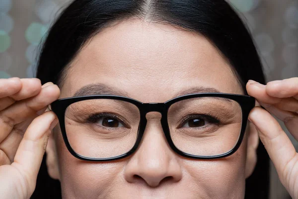Cropped view of asian woman touching eyeglasses and looking at camera, eye care concept — стоковое фото