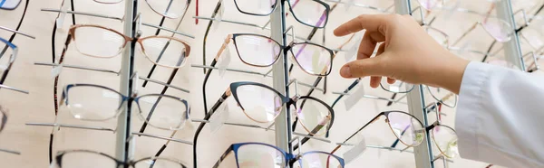 Vista recortada de oculista tomando gafas en la tienda de óptica, banner - foto de stock