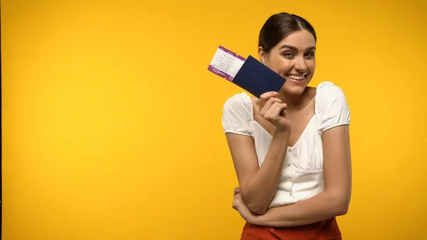 Cheerful tourist holding passport and boarding pass isolated on yellow — стоковое фото