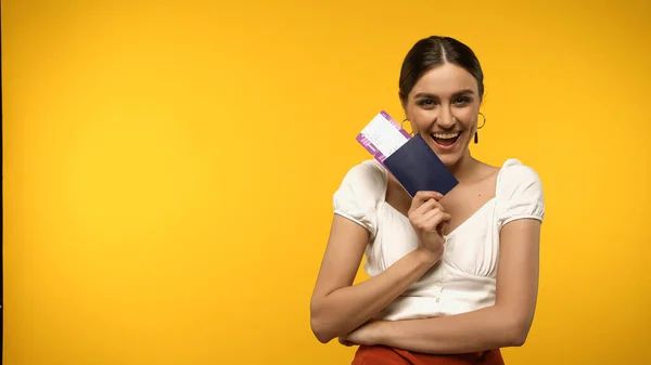 Happy woman holding passport and air ticket while looking at camera isolated on yellow - foto de stock
