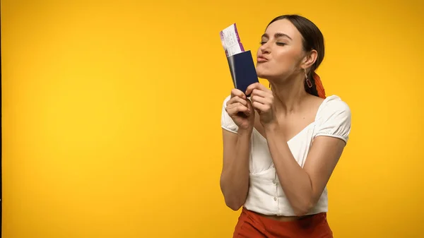 Young woman kissing passport and air ticket isolated on yellow — стоковое фото