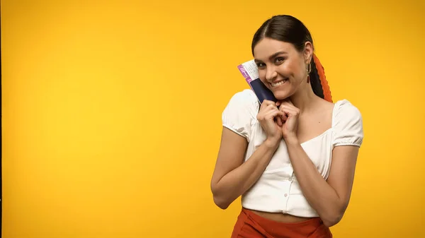 Positive young woman holding passport and air ticket isolated on yellow — Fotografia de Stock