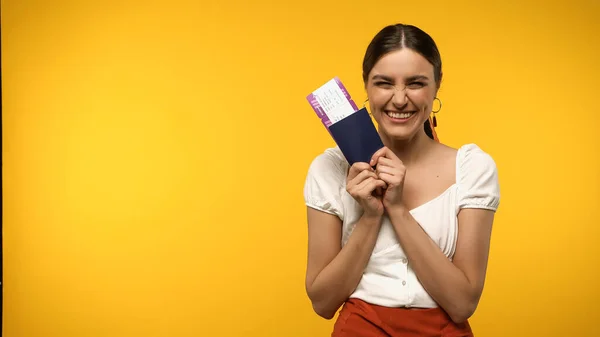Excitado viajero sosteniendo tarjeta de embarque y pasaporte aislado en amarillo - foto de stock
