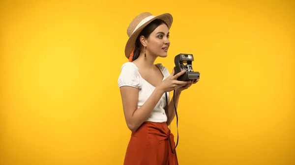 Sorrindo mulher em chapéu de palha segurando câmera vintage isolado no amarelo — Fotografia de Stock