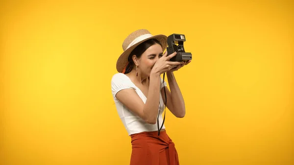 Woman in straw hat taking photo on vintage camera isolated on yellow — Photo de stock